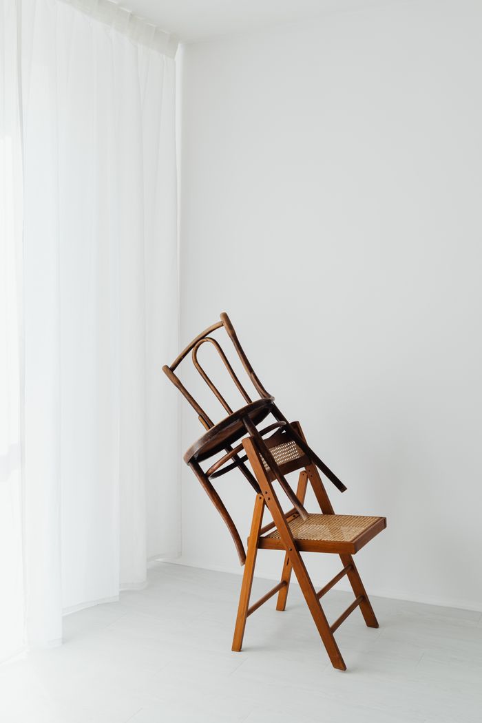 about-02 Artistic composition of two wooden chairs stacked in a minimalist white room.